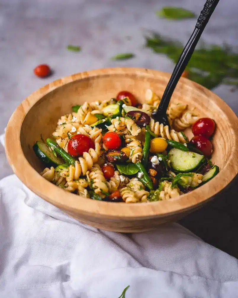 Vegan Mediterranean Pasta Salad 2 Cooking process image showing a bowl of pasta salad with fresh herbs being stirred